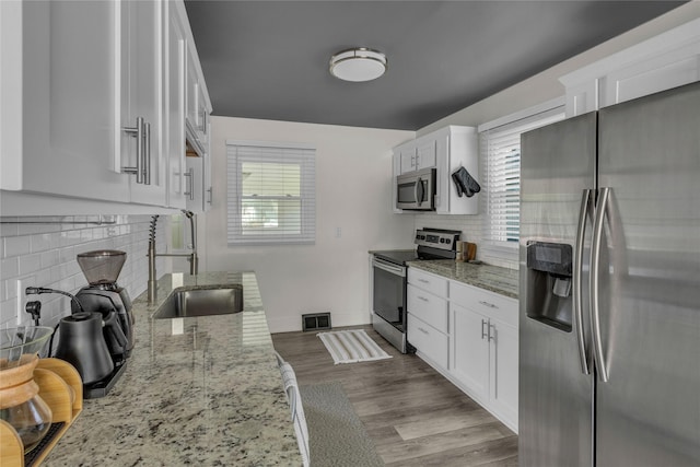 kitchen featuring stainless steel appliances, backsplash, a sink, white cabinets, and light stone countertops