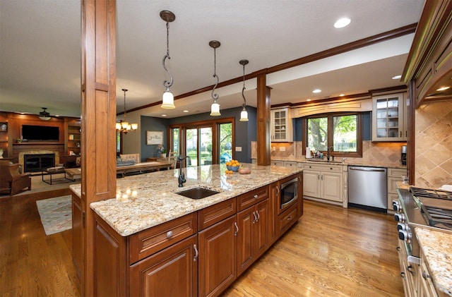 kitchen with a sink, appliances with stainless steel finishes, glass insert cabinets, light stone counters, and ornamental molding