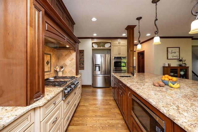 kitchen featuring stainless steel appliances, a sink, cream cabinets, ornamental molding, and light stone counters