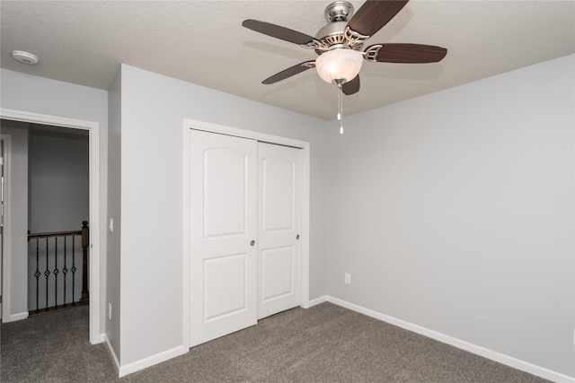 unfurnished bedroom with dark colored carpet, a closet, baseboards, and a ceiling fan
