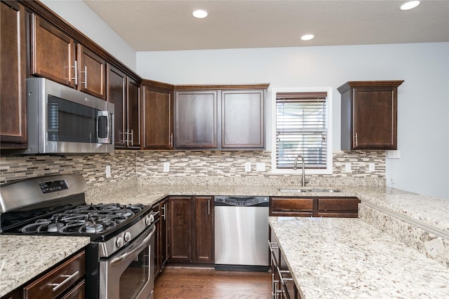 kitchen with appliances with stainless steel finishes, a sink, dark wood-style floors, dark brown cabinets, and decorative backsplash