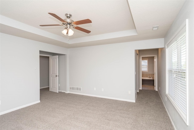 unfurnished bedroom featuring carpet floors, a tray ceiling, baseboards, and ceiling fan