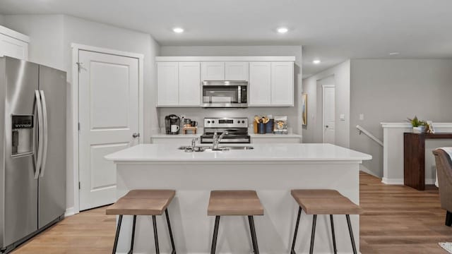 1415 Northview Dr, Waukee, IA 50263 - kitchen with appliances with stainless steel finishes, a breakfast bar, white cabinetry, light wood-type flooring, and recessed lighting
