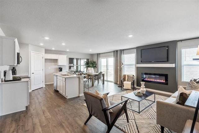 living area with a glass covered fireplace, dark wood finished floors, healthy amount of natural light, recessed lighting, and a textured ceiling