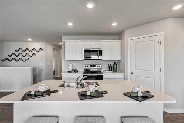 kitchen featuring stainless steel appliances, a sink, white cabinets, a breakfast bar area, and recessed lighting