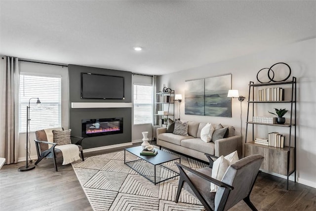living area featuring healthy amount of natural light, baseboards, wood finished floors, a glass covered fireplace, and recessed lighting