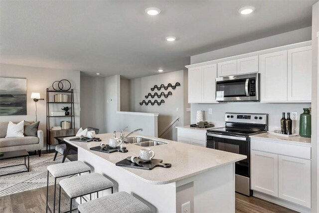 kitchen with stainless steel microwave, range with electric cooktop, a sink, dark wood-style flooring, and a center island with sink
