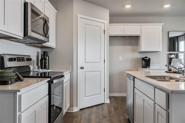 kitchen with appliances with stainless steel finishes, a sink, dark wood-type flooring, white cabinets, and light stone counters