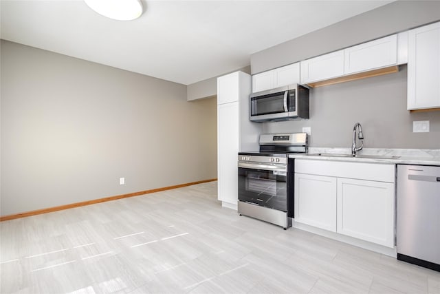 kitchen featuring stainless steel appliances, a sink, light countertops, white cabinetry, and baseboards