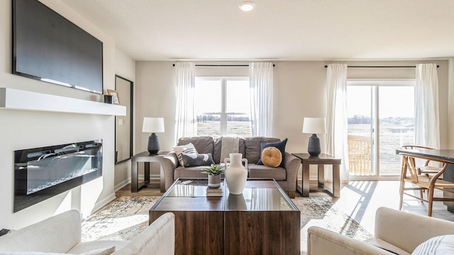 living room featuring plenty of natural light, a glass covered fireplace, wood finished floors, and baseboards