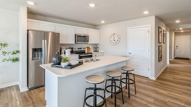 kitchen with appliances with stainless steel finishes, white cabinetry, light wood finished floors, a breakfast bar, and light countertops