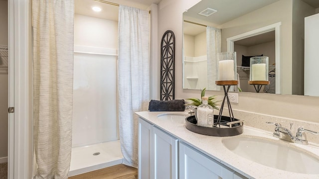 full bath with a stall shower, double vanity, and wood finished floors