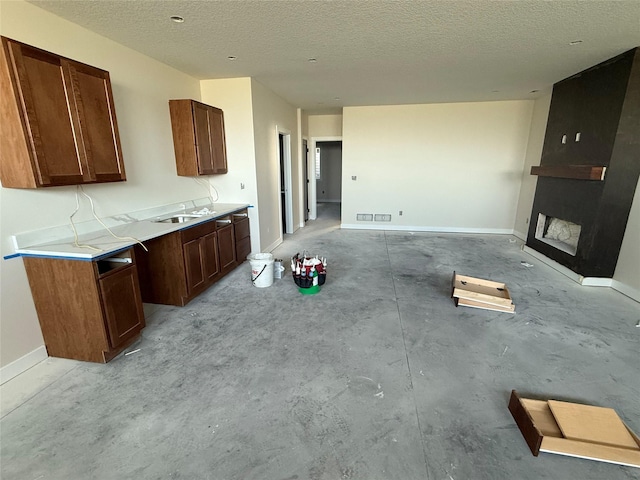 kitchen featuring a large fireplace, a textured ceiling, baseboards, light countertops, and open floor plan