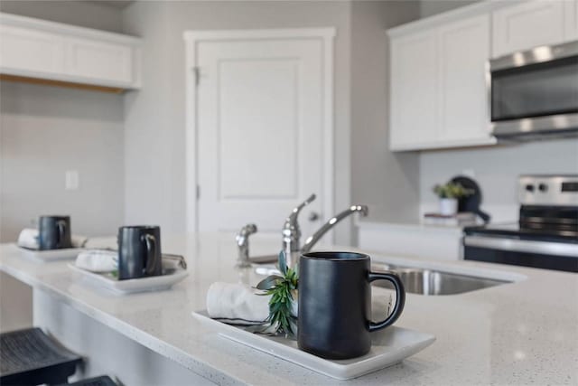 kitchen with stainless steel appliances, white cabinetry, a sink, and light stone countertops