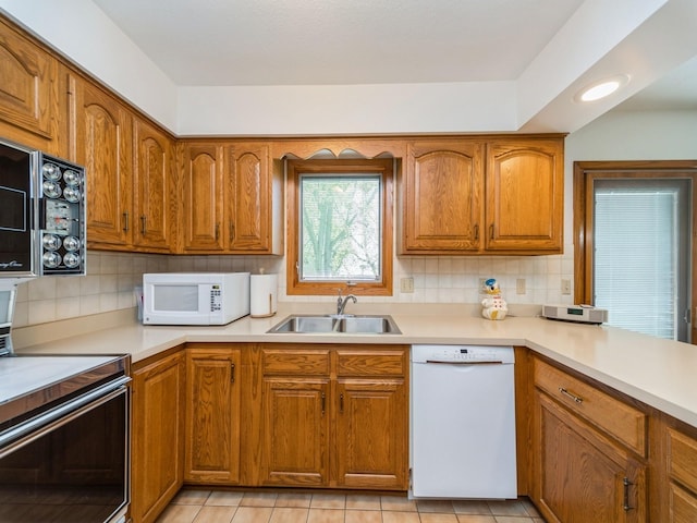 kitchen with white appliances, a sink, brown cabinetry, light countertops, and tasteful backsplash