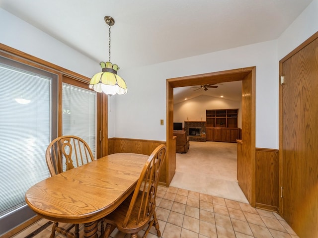 dining room with a wainscoted wall, wooden walls, light colored carpet, a fireplace, and ceiling fan