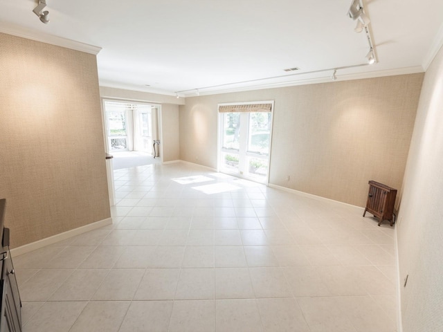spare room with track lighting, ornamental molding, healthy amount of natural light, light tile patterned floors, and baseboards
