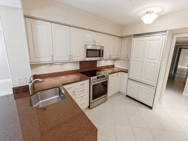 kitchen featuring appliances with stainless steel finishes, a sink, wallpapered walls, dark countertops, and white cabinets