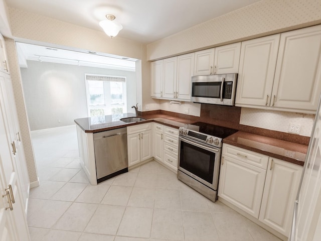 kitchen featuring stainless steel appliances, dark countertops, a sink, light tile patterned floors, and wallpapered walls