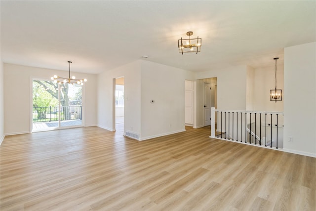 spare room featuring a chandelier, light wood-style flooring, and baseboards