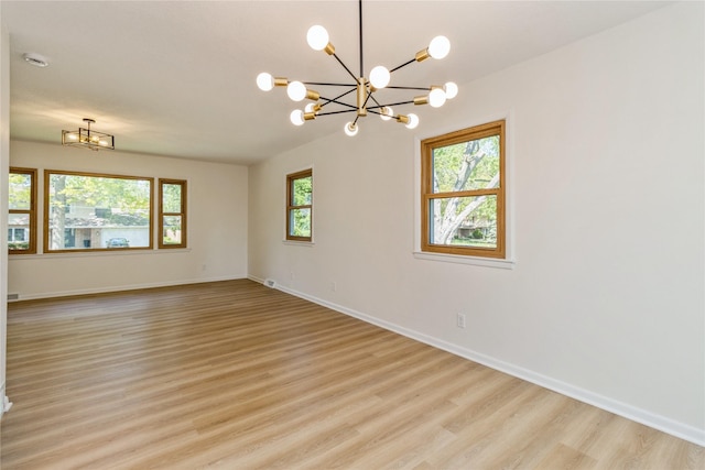 spare room featuring a chandelier, light wood-style flooring, and baseboards