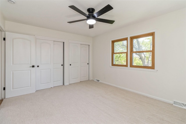 unfurnished bedroom with multiple closets, baseboards, light colored carpet, and a ceiling fan