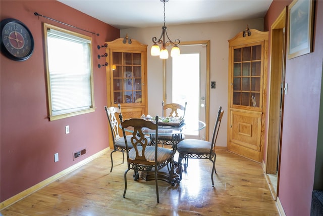 dining space with light wood-style flooring, a chandelier, and baseboards