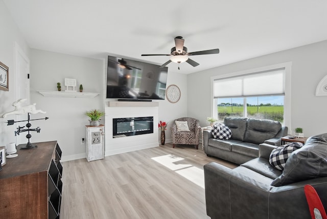 living area with light wood-type flooring, a ceiling fan, a glass covered fireplace, and baseboards
