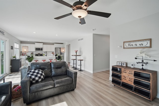 living area featuring light wood-type flooring, a ceiling fan, baseboards, and recessed lighting