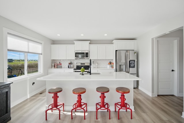 kitchen with appliances with stainless steel finishes, a sink, a center island with sink, a breakfast bar area, and light countertops