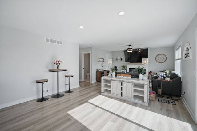 kitchen with ceiling fan, light wood-style flooring, baseboards, a glass covered fireplace, and recessed lighting