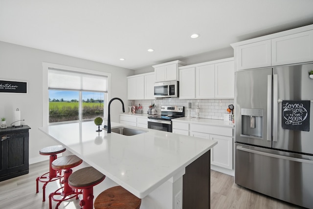 kitchen with appliances with stainless steel finishes, a sink, decorative backsplash, light wood-type flooring, and an island with sink