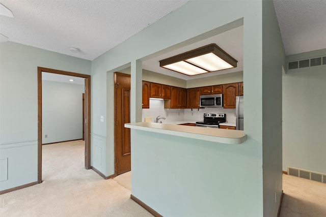 kitchen featuring stainless steel appliances, light colored carpet, light countertops, a textured ceiling, and a peninsula