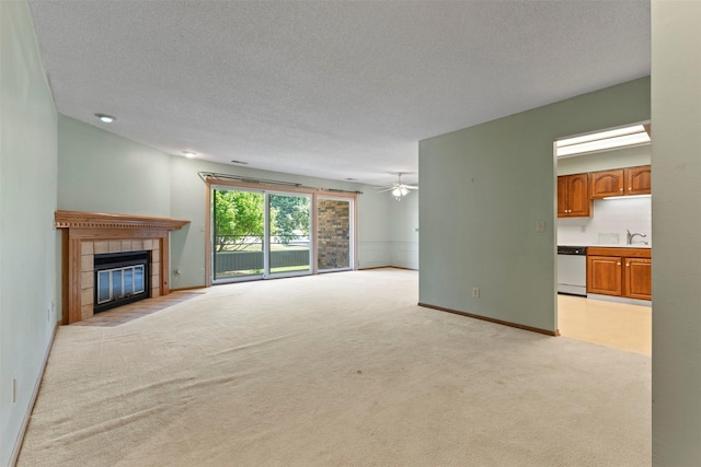 unfurnished living room with a tile fireplace, light colored carpet, a textured ceiling, ceiling fan, and a sink