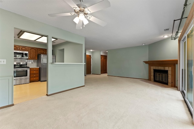 unfurnished living room with light carpet, a tile fireplace, baseboards, and ceiling fan