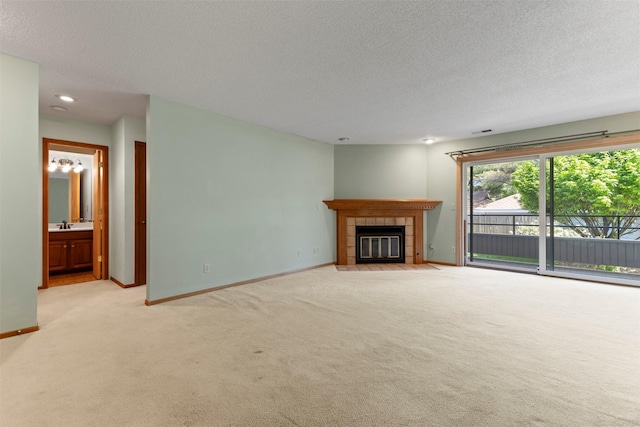 unfurnished living room featuring light carpet, a textured ceiling, baseboards, and a tiled fireplace