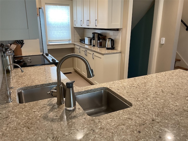 kitchen featuring a sink, white cabinetry, light stone countertops, and decorative backsplash