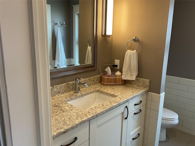 bathroom featuring tile walls, vanity, toilet, a wainscoted wall, and tile patterned floors