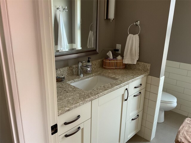 bathroom with a wainscoted wall, tile walls, tile patterned flooring, vanity, and toilet