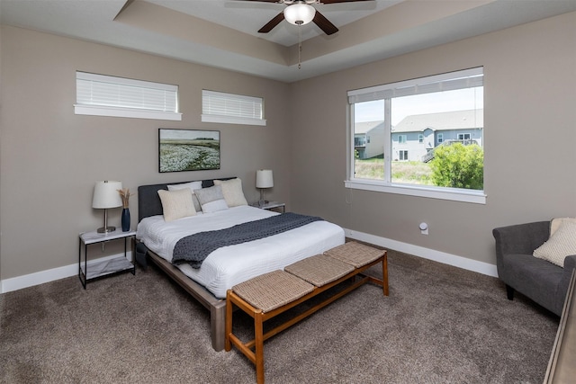 bedroom featuring a raised ceiling, carpet flooring, baseboards, and a ceiling fan