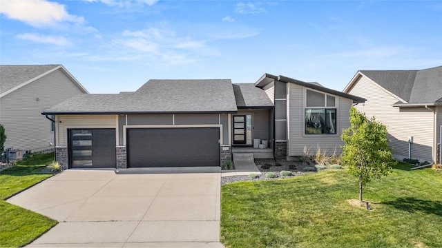 view of front of house with an attached garage, driveway, a front lawn, a shingled roof, and stone siding