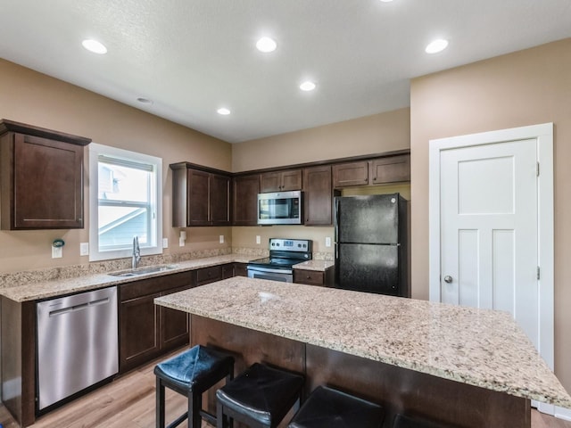 kitchen with appliances with stainless steel finishes, a sink, dark brown cabinets, a breakfast bar, and light wood finished floors