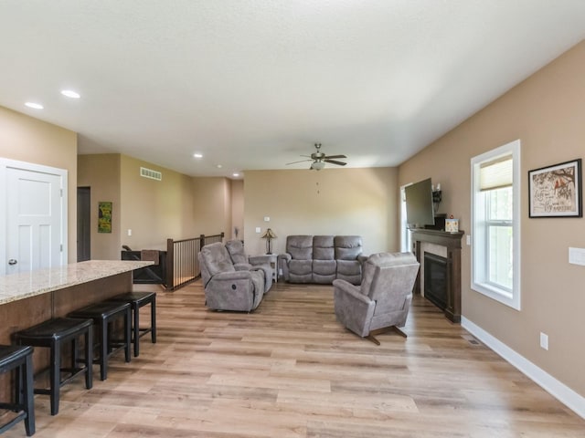 living area with light wood finished floors, ceiling fan, a glass covered fireplace, recessed lighting, and baseboards