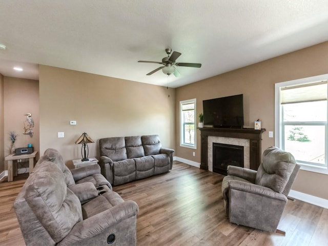 living room featuring baseboards, wood finished floors, a ceiling fan, and a fireplace