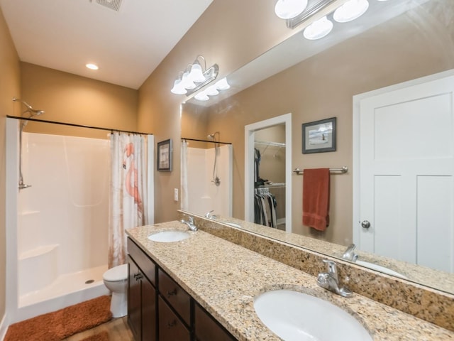 bathroom featuring a stall shower, toilet, double vanity, a walk in closet, and wood finished floors