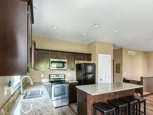 kitchen with stainless steel appliances, a sink, a center island, dark wood-type flooring, and dark brown cabinetry
