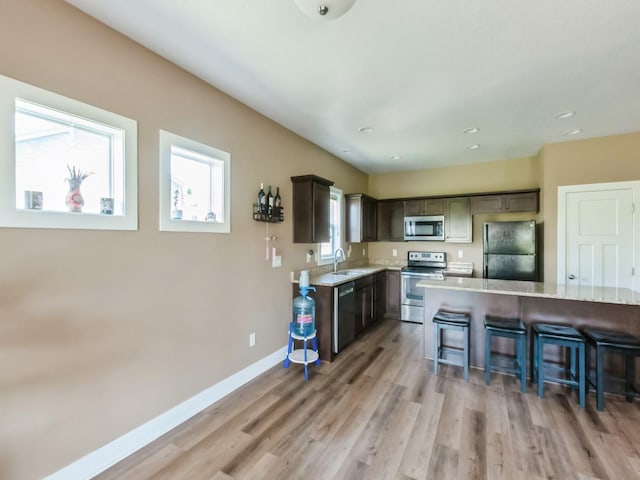kitchen with black appliances, a sink, a kitchen bar, light wood-type flooring, and baseboards