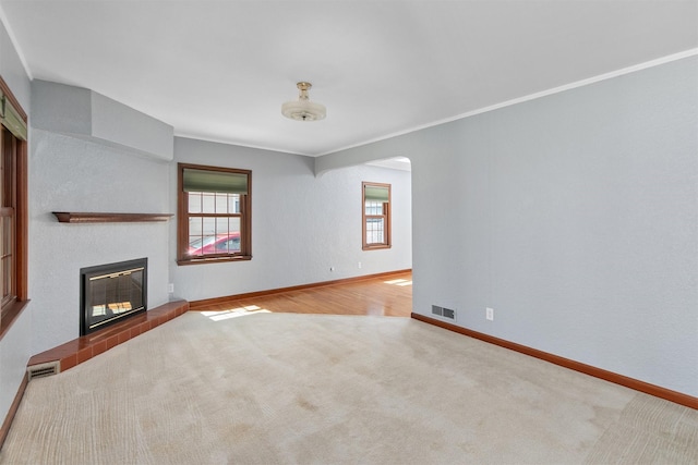 2400 39th St, Des Moines, IA 50310 - unfurnished living room with carpet floors, arched walkways, a glass covered fireplace, baseboards, and crown molding