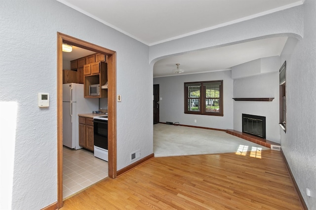 2400 39th St, Des Moines, IA 50310 - unfurnished living room featuring a textured wall, a glass covered fireplace, crown molding, arched walkways, and light wood-style floors