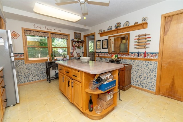 kitchen featuring light flooring, freestanding refrigerator, wallpapered walls, a ceiling fan, and light countertops